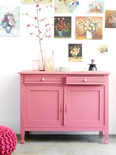 a pink dresser with pictures on the wall and flowers in vases sitting on top