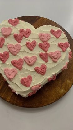 a heart shaped cake sitting on top of a wooden cutting board with pink and white frosting