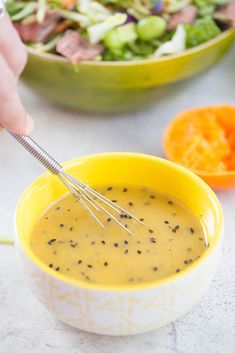 a person holding a whisk over a bowl of soup with salad in the background