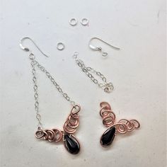 two pairs of earrings are shown on a white surface with silver chains and black stones