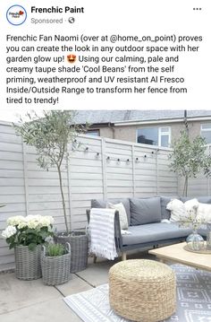 an outdoor living room with grey furniture and white flowers on the table, in front of a fence