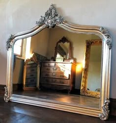 an ornate silver framed mirror sitting on top of a wooden floor next to a dresser