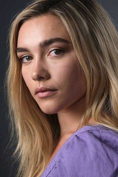 a woman with long blonde hair and blue eyes is looking at the camera while wearing a purple shirt