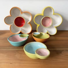 several bowls with flower designs on them sitting on a wooden table next to a white wall