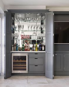 a kitchen with gray cabinets and shelves filled with bottles, wine glasses, and utensils