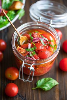 a jar filled with tomatoes and onions on top of a wooden table next to fresh basil leaves