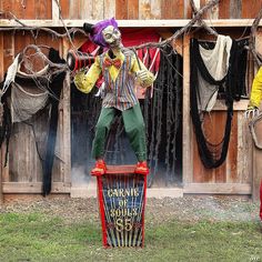 a creepy clown standing on top of a trash can in front of a wooden building