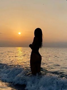 a woman standing in the ocean at sunset