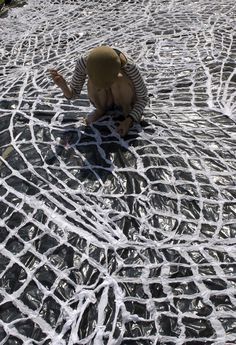 a person kneeling down on the ground in front of a netted area with trees