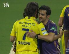 two men are embracing each other on the field during a game in india, one is wearing a yellow jersey and the other has a purple shirt that says ethad airways