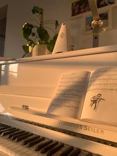 an open book sitting on top of a white piano next to a potted plant