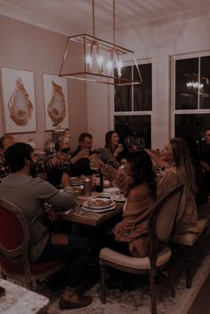 a group of people sitting around a dining room table with food and wine glasses in their hands