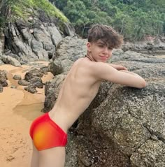 a young man leaning against a rock on the beach with his arm resting on it