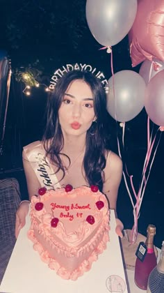 a woman sitting at a table with a heart shaped cake and balloons in the background