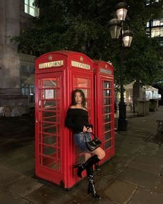 a woman standing next to a red phone booth