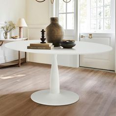 a white table with a vase on it and some books in front of the window