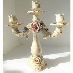 an ornate white candle holder with flowers on it's sides and four candles in the middle