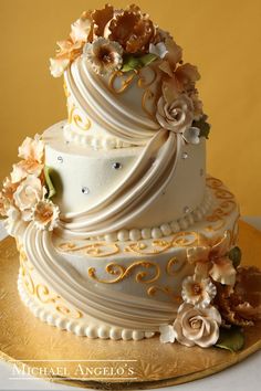 a three tiered wedding cake with flowers on top sits on a gold platter