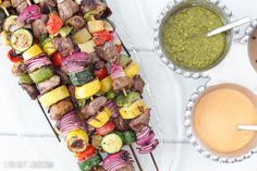 skewers of vegetables and meat are on the grill next to a bowl of pesto sauce