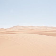 two people walking in the desert with sand dunes behind them and a blue sky above