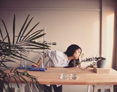 a woman sitting at a table with a plant in front of her and looking up