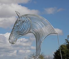 a large metal horse statue sitting on top of a lush green field under a blue cloudy sky