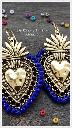 Oriana Earrings Materials:  Sterling Silver plated hooks, Silver over Pewter Heart, Czech Glass, 10k plated Gold hooks, Gold over Pewter Heart Length:  2.5" Milagro flaming hearts Inspired by Mexican Folk Art & the colorful embroidery crafted throughout Latin America.  The Oriana earrings shown in beautiful Indigo Dark Blue Czech Glass beads around these gorgeous gold hearts.  Choose from either Silver or Gold Hearts.   Shown here are is the Indigo color.  You can choose from solid colors:  Red, Orange, Yellow, Green, Blue, Indigo (Dark Blue), Violet, Black, or White.  Also available in Rainbow.   Feel free to message me if you would like to request a custom color or color combination.   The sacred heart is a symbol of everlasting love & commitment. Your earrings will be very similar to th Mexican Jewelry Gold Mexico, Sacred Heart Earrings, Sacred Heart Art, Mexican Lace, Sacred Jewelry, Tin Ornaments, Mexican Gifts, Mexican Crafts, Diy Jewelry Inspiration