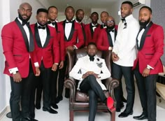 a group of men in red tuxedos posing for a photo with one man sitting on a chair