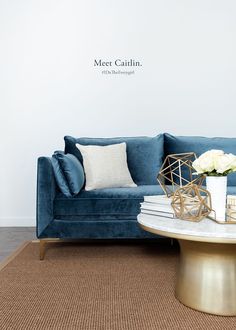 a living room with a blue velvet couch and coffee table in front of a white wall