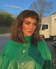 a woman wearing a green leather jacket standing in front of a truck