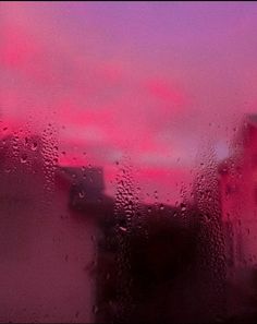 rain drops on the window with buildings in the background and pink clouds behind it at dusk