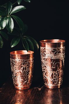 two copper cups sitting on top of a wooden table