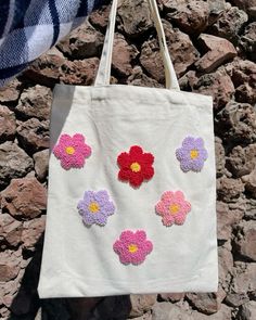 a white bag with crocheted flowers on it hanging from a stone wall next to a person's hand