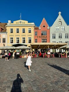 a woman is standing in the middle of an open air market area with many colorful buildings