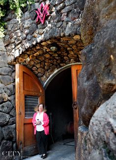 a woman standing in front of a stone building with an arched doorway and wooden door