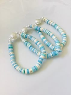 three stranded necklaces with blue and white beads on a white surface, one is wearing a silver clasp