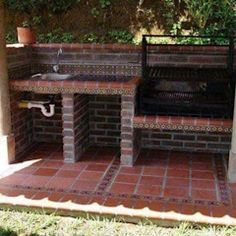 an outdoor grill made out of bricks in the yard with a sink and bench on it