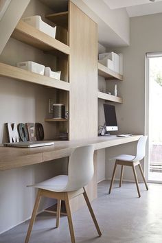 a desk with two chairs and a laptop on it in front of a wall mounted bookcase