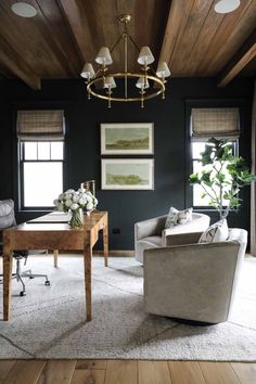 a living room filled with furniture and a chandelier above a wooden table in front of two windows