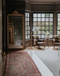 a living room with two chairs and a rug in front of a large mirror on the wall