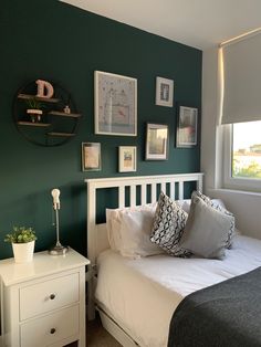 a bedroom with green walls and pictures on the wall above the bed, along with a white dresser