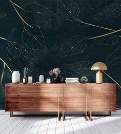 a wooden sideboard sitting on top of a white floor next to a wall covered in leaves