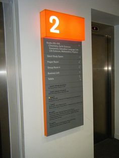 an orange and gray sign on the wall next to a metal door with numbers in it