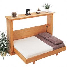 a wooden bed frame with two pillows on it and a plant in the corner next to it