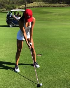 a woman is playing golf on the green with other people in the car behind her