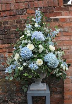 a vase filled with blue and white flowers next to a brick wall