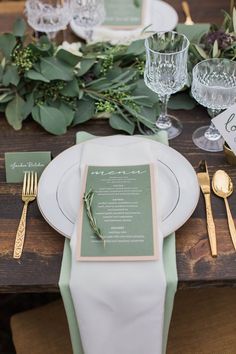 the table is set with silverware and greenery