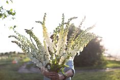 a woman holding a bouquet of flowers in her hands while standing on a grass covered field