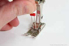 a hand is holding a sewing machine with red pins on the side and white background