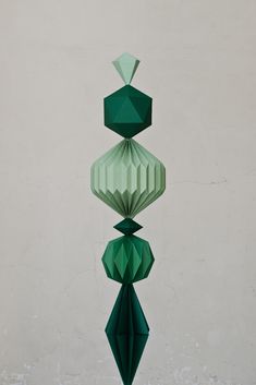 an abstract sculpture made out of green paper hanging from the ceiling in front of a white wall